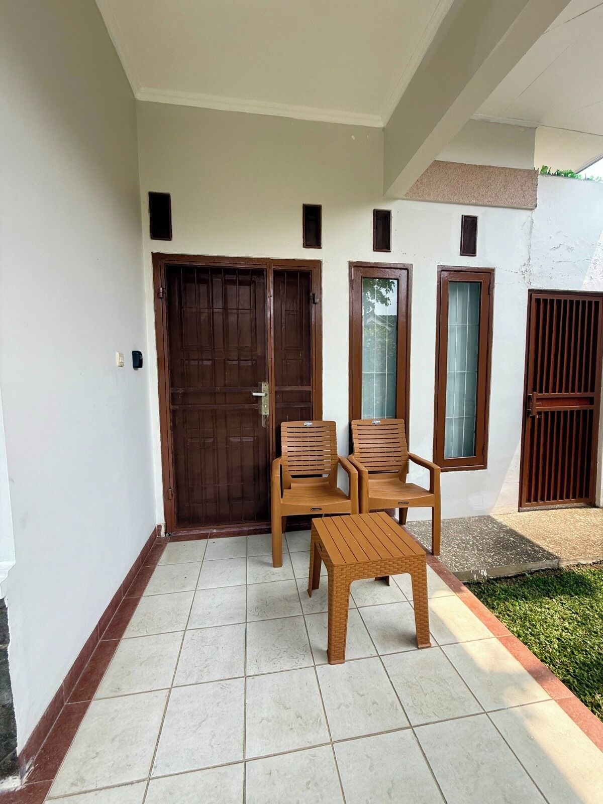 A covered patio area with a tiled floor, two wooden chairs, a small wooden table, and a large wooden door.