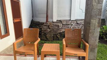 Dos sillas de madera y una pequeña mesa en un patio con paredes de piedra y una ventana con persianas.