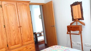 Une chambre avec une armoire en bois, un miroir sur pied et un lit recouvert d’une couvre-lit à motifs.