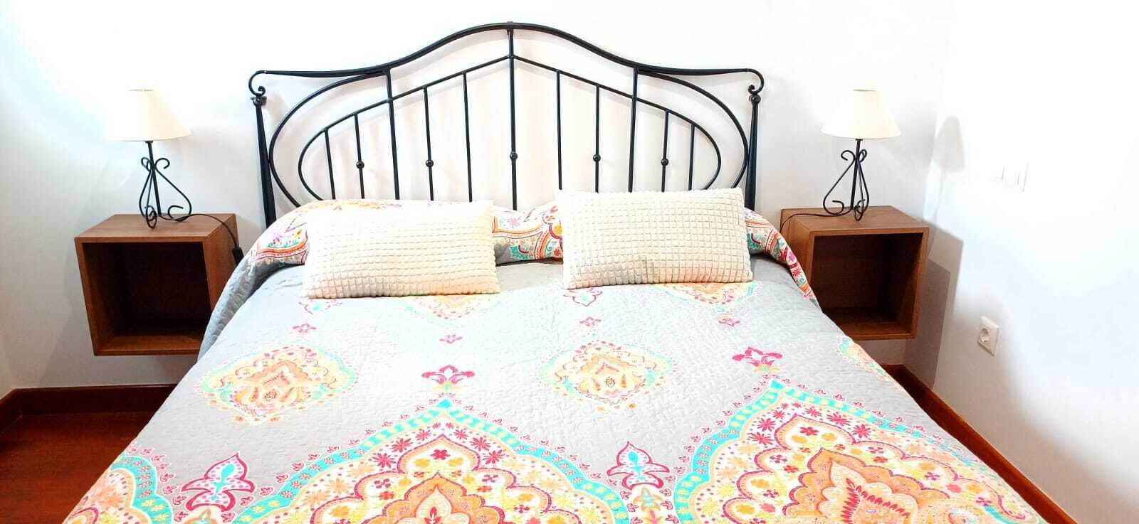 Een bed met een gebedruid sprei, twee kussens en twee nachtkastjes met lampen.