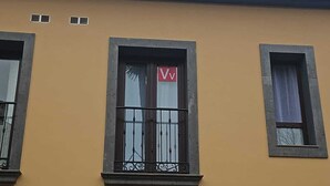 Un bâtiment à la façade jaune, doté de nombreuses fenêtres avec des grilles métalliques, et d’un panneau rouge en forme de « V » sur l’une des fenêtres.