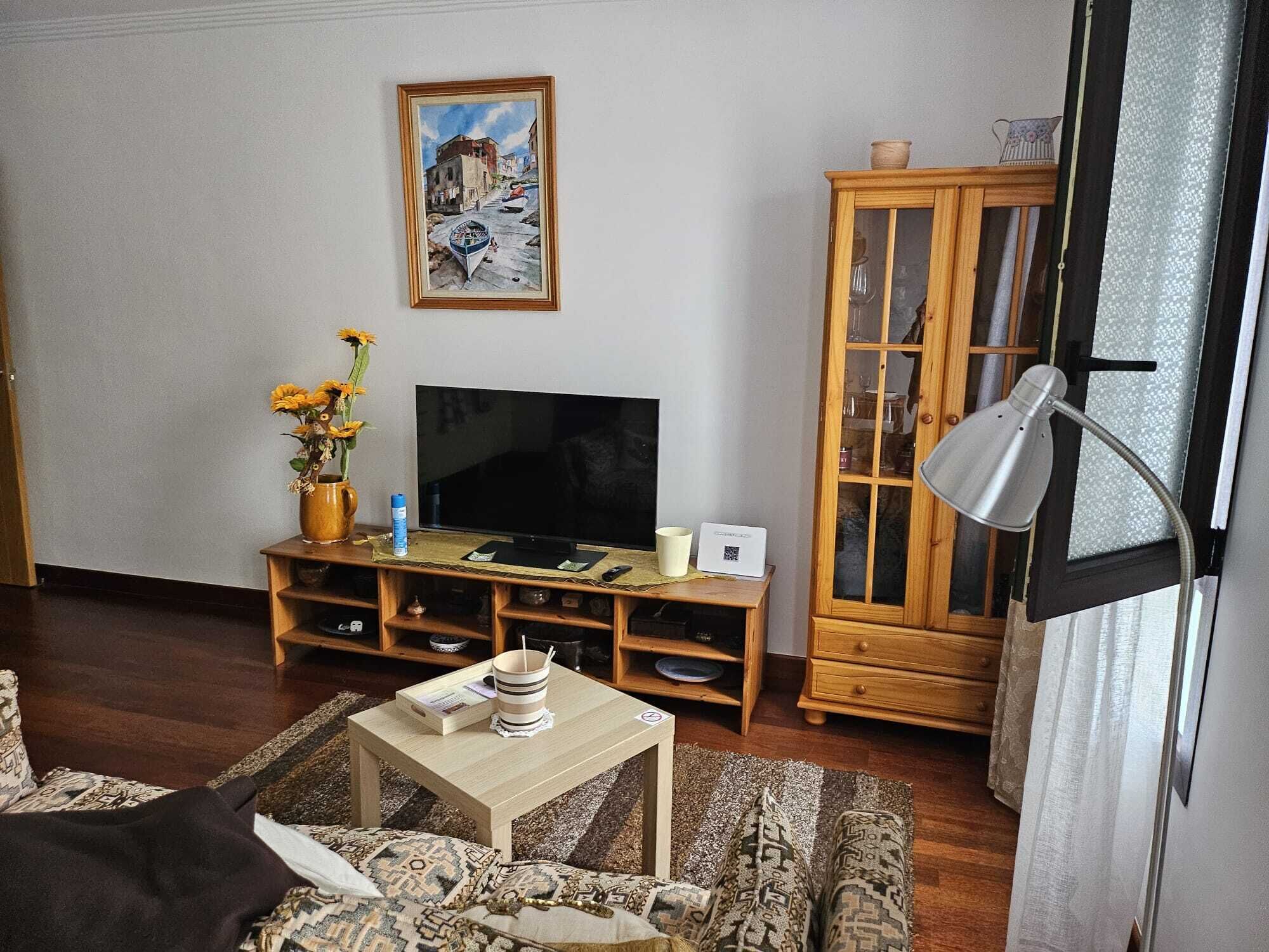 Una sala de estar con televisor, aparador de madera y un cuadro en la pared.