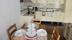 Une cuisine compacte avec des meubles de couleur claire, un petit plan de travail et un coin repas comprenant une table en bois pour quatre personnes.