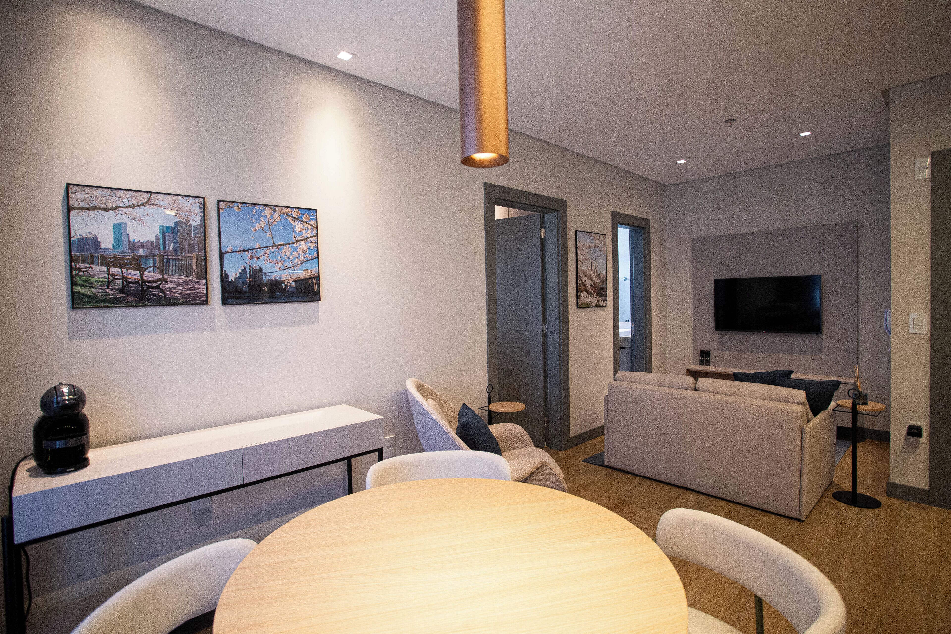 A modern living room with a dining area, a sofa, a TV, and artwork on the walls.