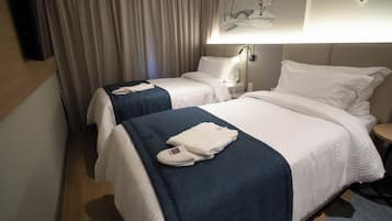 Habitación de hotel con dos camas, un televisor de pantalla plana, un cuadro en la pared y una mesita de noche con lámpara.