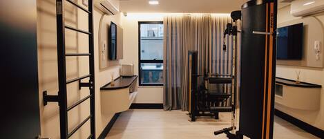 Habitación de hotel con barra de dominadas, equipo de ejercicios, televisor y ventana con cortinas.