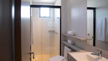 Un bany modern amb porta de vidre per a la dutxa, un vàter, un rentapeus i un mirall.