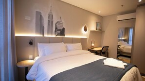 A hotel room with a large bed, a desk, and a chair. There is a painting on the wall and an air conditioning unit above the bed. - Nobile Grand Itapema (Itapema)