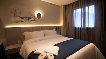 Una cama bien hecha con sábanas blancas, una manta azul oscuro y un par de pantuflas sobre la cama.