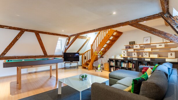 A loft-style living room with exposed wooden beams, a pool table, a staircase, and a cozy seating area. - Le Cocon Alsacien - Appt authentique coeur strasbourg (Strasbourg)