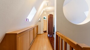 A narrow hallway with wooden flooring and a wooden railing on one side. There is a circular light fixture on the wall and a small window on the left. - Le Cocon Alsacien - Appt authentique coeur strasbourg (Strasbourg)