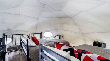 A spacious tent with two beds, each with a pillow and a blanket. There is a small stool and a bench with a metal frame.