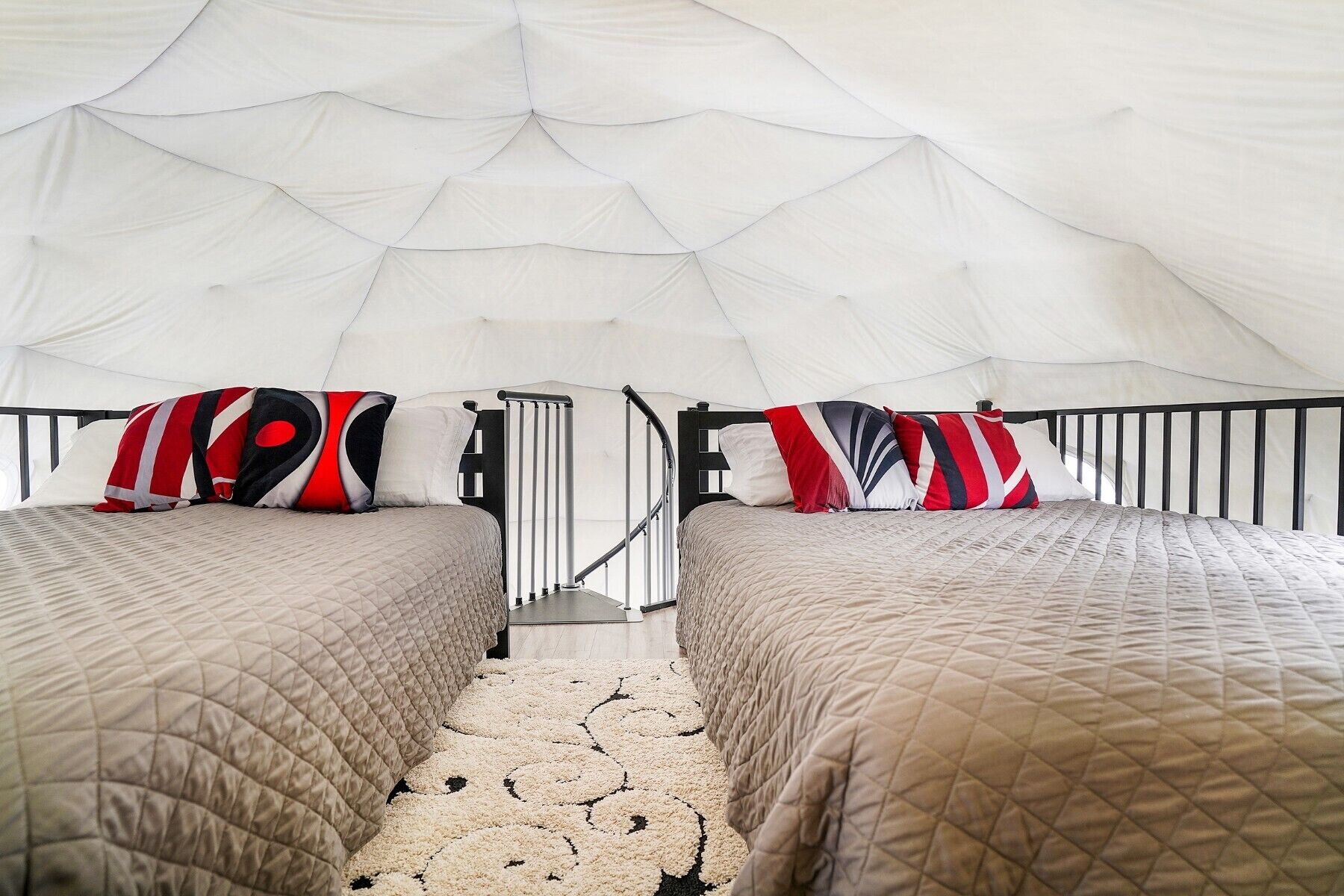 Two beds in a tent with a patterned carpet and a metal railing.