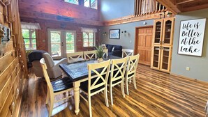 A cozy cabin interior with a dining area, wooden walls, and a large window overlooking greenery.