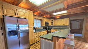 A modern kitchen with wooden cabinets, a stainless steel refrigerator, a built-in oven, and a large island with bar stools.