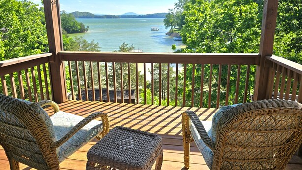 A wooden deck with wicker furniture overlooking a lake.