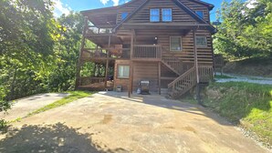 A two-story wooden cabin with a balcony, a covered porch, and a concrete driveway.