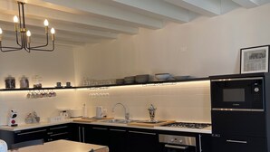 A modern kitchen with a black countertop, stainless steel appliances, and a wooden dining table with chairs. - Residence19 ilborgo (Asolo)