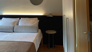 A bedroom with a bed, a round light fixture, a small table, and a door leading to another room. - Residence19 ilborgo (Asolo)