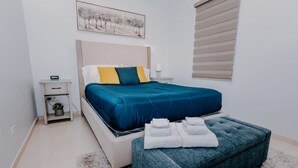 Un dormitorio con cama, mesita de noche, lámpara y un cuadro en la pared.