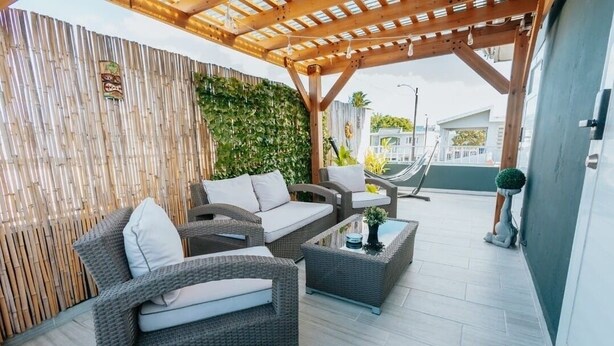 Un patio exterior con mobiliario de mimbre, una pérgola de madera y una pared de bambú.