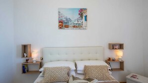 Ein Schlafzimmer mit einem weißen Bett, zwei Nachttischen, einem Wandbild und einem kleinen Regal mit einer Schmetterlingsdekoration.