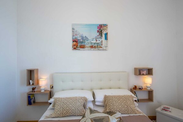 Une chambre avec un lit blanc, deux tables de chevet, un tableau accroché au mur et une petite étagère décorée d’un motif de papillon.