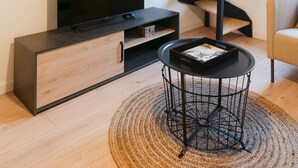 Un salon moderne avec un escalier en colimaçon, un téléviseur à écran plat, un meuble en bois et une table basse ronde.