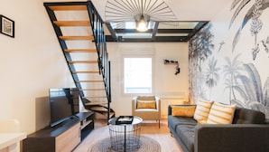 Un salon moderne avec un escalier en bois, un téléviseur à écran plat, une table basse ronde et un canapé agrémenté de coussins à rayures.