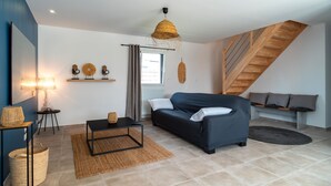 A modern living room with a dark blue sofa, a black coffee table, a woven rug, and a wooden staircase.