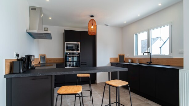 A modern kitchen with a central island, black cabinets, and a window providing natural light.