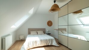 A bedroom with a sloped ceiling, a bed with a headboard, a round woven light fixture, and a large mirror on the wall.