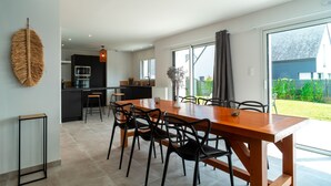 A modern kitchen with a central island, a dining area with a wooden table and black chairs, and large windows offering a view of the outdoors.