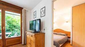 Ein Schlafzimmer mit einem hölzernen Bett, einem Fernseher auf einer Holzkommode und einem Fenster mit Vorhängen.