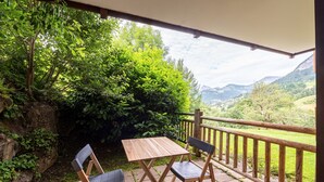 Eine Terrasse im Freien mit Holztisch und zwei Stühlen, umgeben von üppiger Vegetation und einem herrlichen Bergblick.