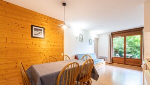 Ein Zimmer mit Holzwand, einem Esstisch mit Stühlen, einem Bett und einem Fenster mit Blick ins Grüne.