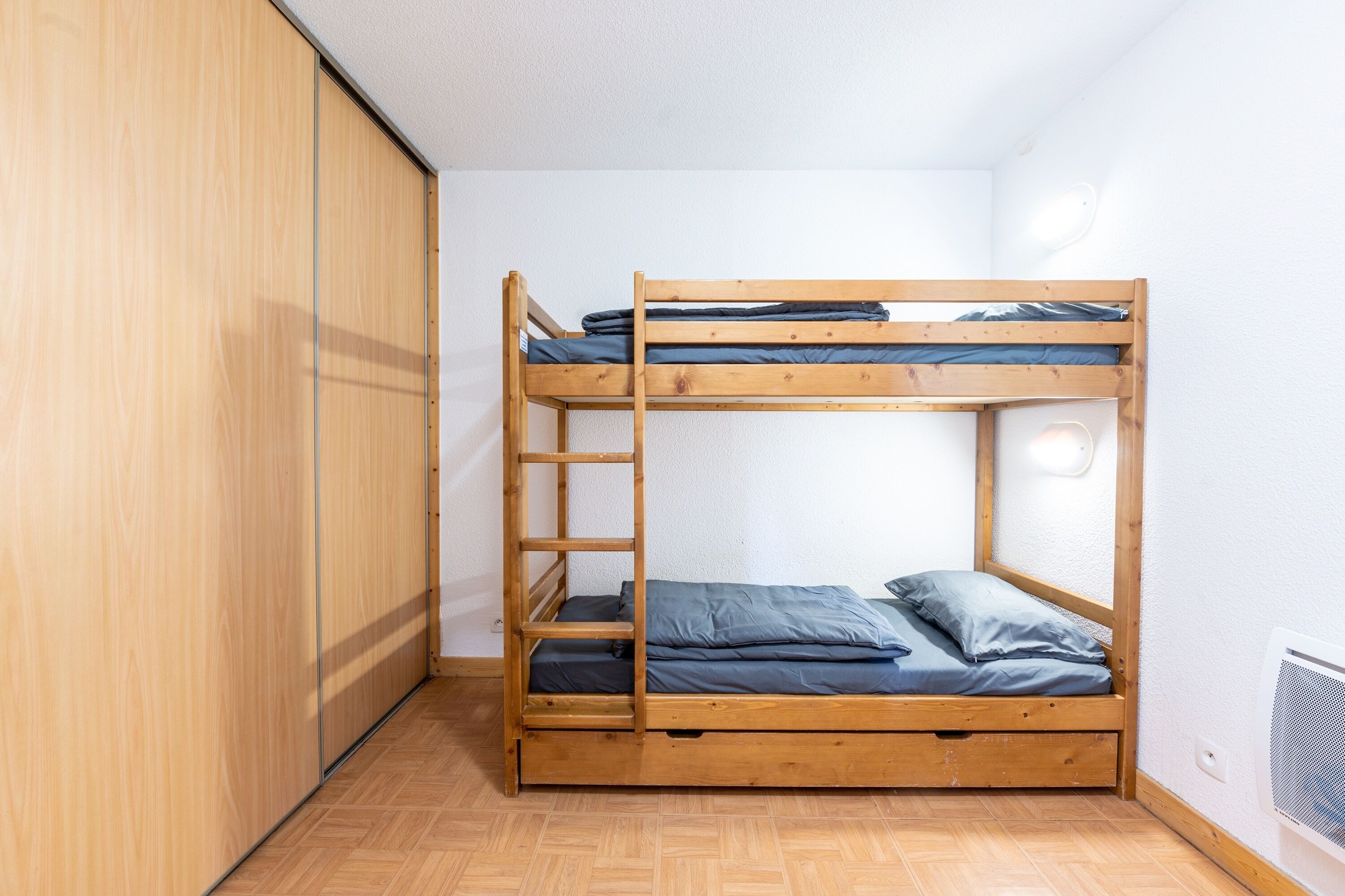 Ein Stockbett in einem Zimmer mit Holzdielen und einem Kleiderschrank.
