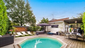 A wooden deck with a swimming pool, outdoor seating, and a covered area with a grill.