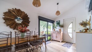 A dining area with a wooden table and chairs, a large mirror, wicker pendant lights, and a view of the outdoors through a glass door.