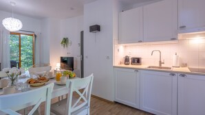 Una cocina moderna con armarios blancos, una mesa de comedor con sillas, una lámpara colgante y un ventanal con cortinas.
