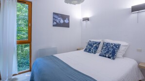 Un dormitorio con cama, ventana con cortinas, una lámpara de pared e imagen en la pared.