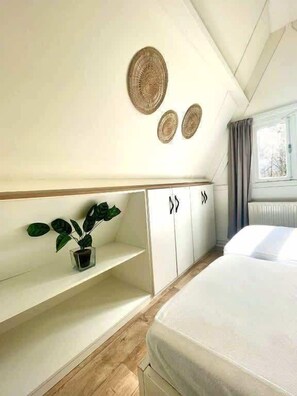 Un dormitorio con una cama, un estante con una planta y tres adornos de pared hechos con fibras.
