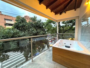 A balcony with a glass railing, a hot tub, and a view of a busy street with cars and trees. - URBANITY LIVING (Medellín)