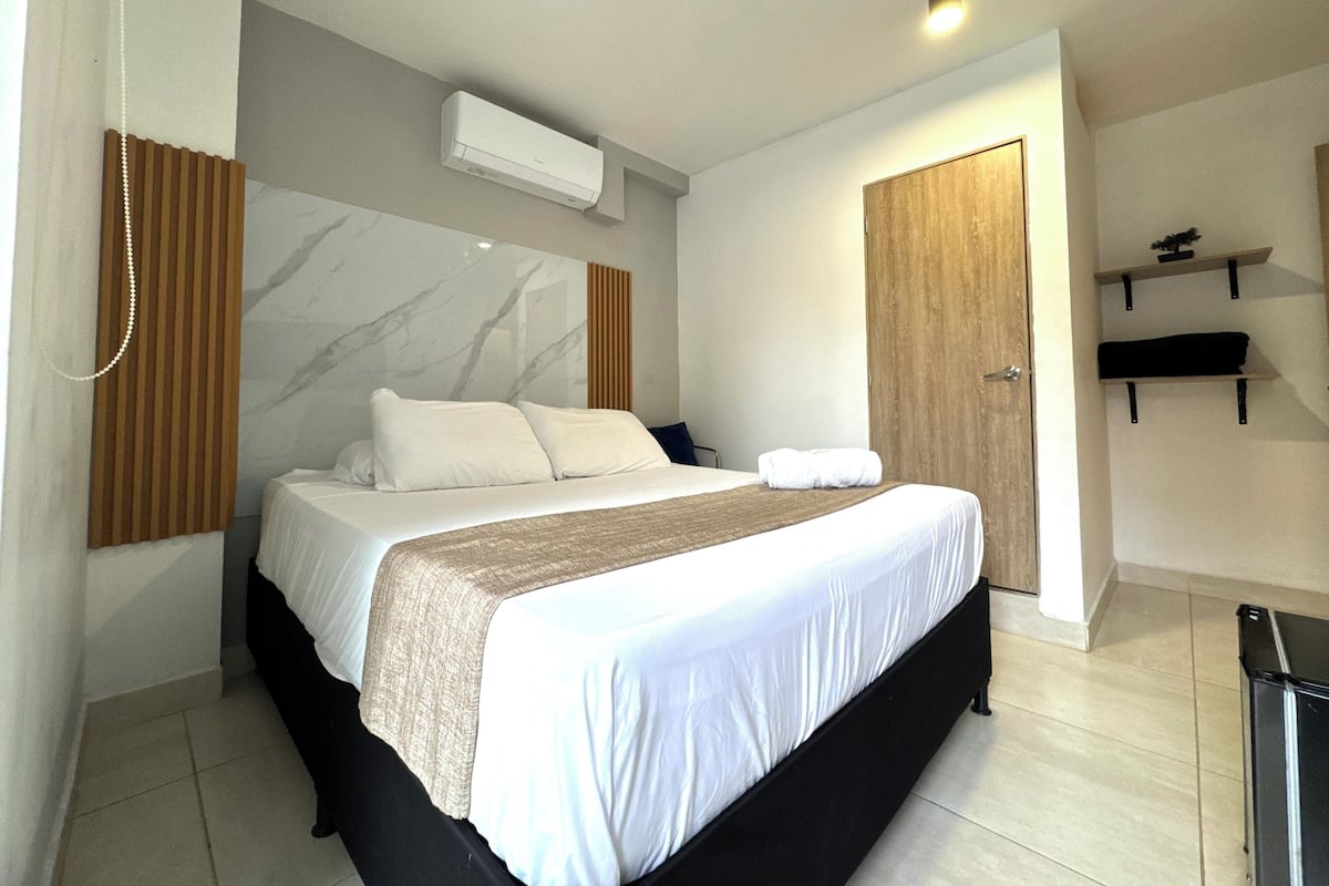 Une chambre d’hôtel moderne avec un grand lit, une porte en bois, une petite étagère et un mur en marbre.