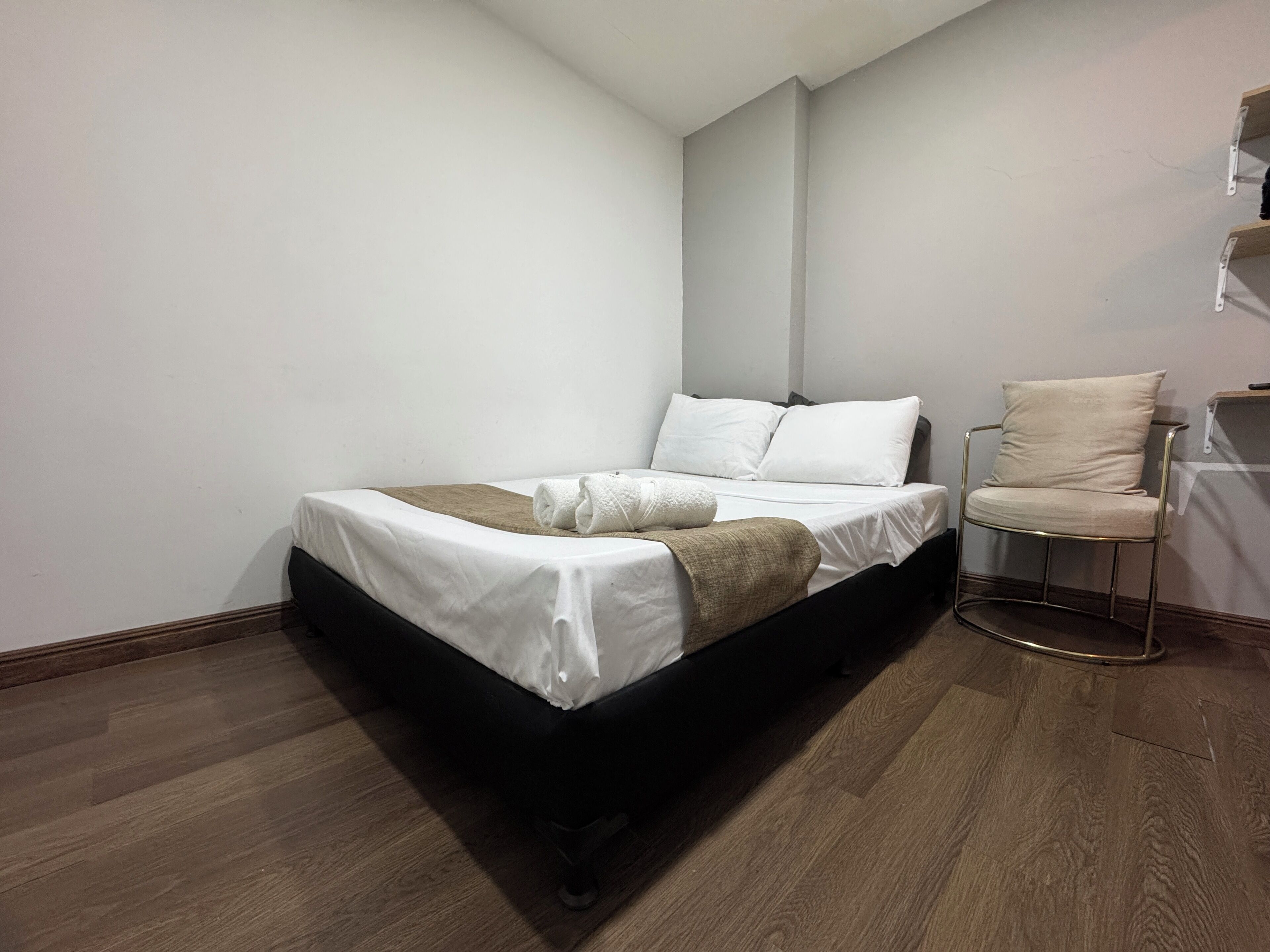 A bedroom with a bed, a chair, and a wooden floor.