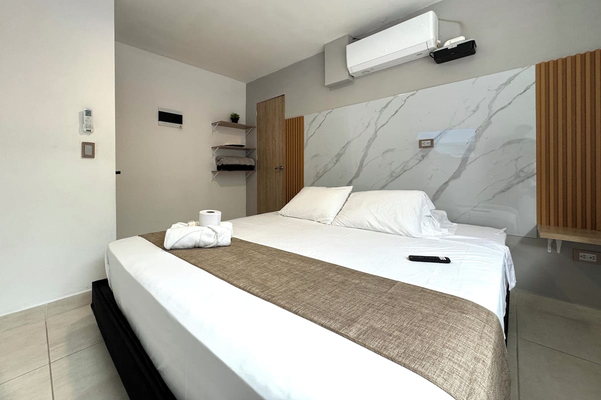 Une chambre d’hôtel équipée d’un lit, d’un climatiseur fixé au mur, d’un téléphone et d’une étagère avec des serviettes.