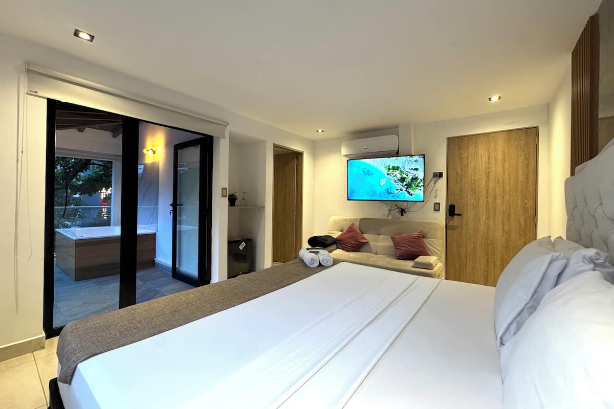 Une chambre d’hôtel moderne dotée d’un grand lit, d’un téléviseur fixé au mur et d’une porte-fenêtre coulissante donnant sur un espace extérieur.
