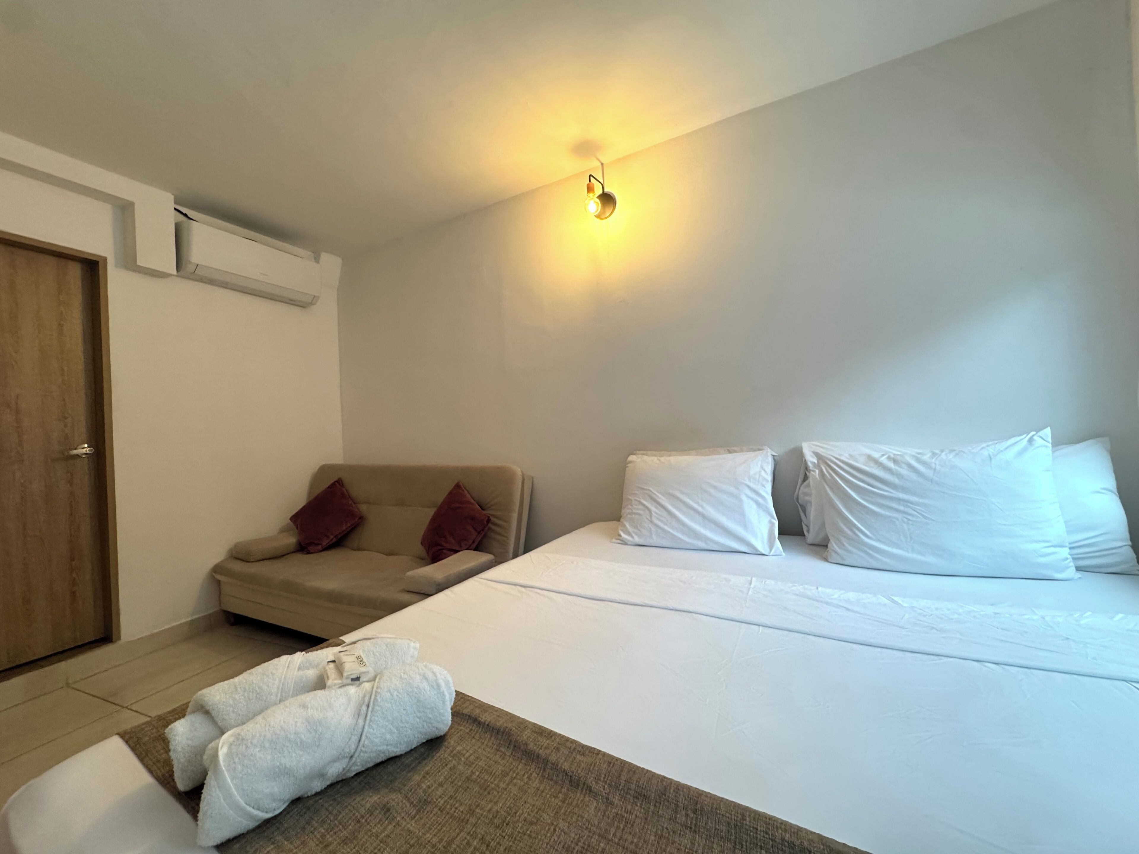 A hotel room with a bed, a sofa, a wall-mounted light, and a door.