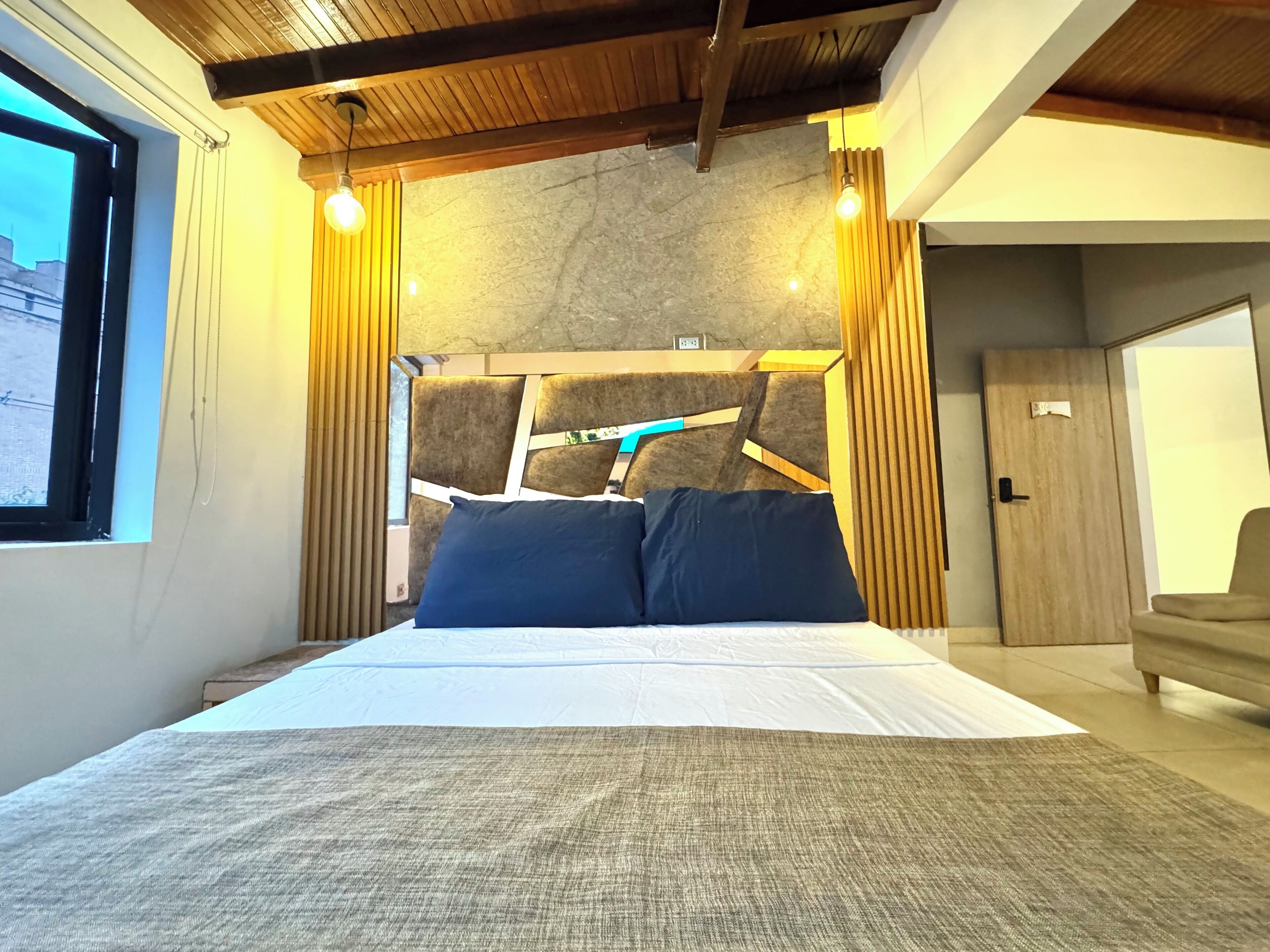 A modern bedroom with a large bed, wooden headboard, and a view of the city through a window.