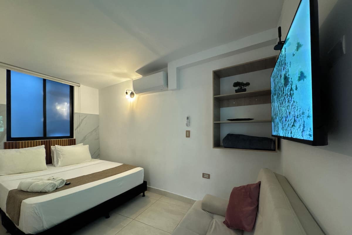Une chambre d’hôtel moderne, équipée d’un lit, d’un canapé, d’un téléviseur fixé au mur et d’une fenêtre donnant sur un paysage agréable.